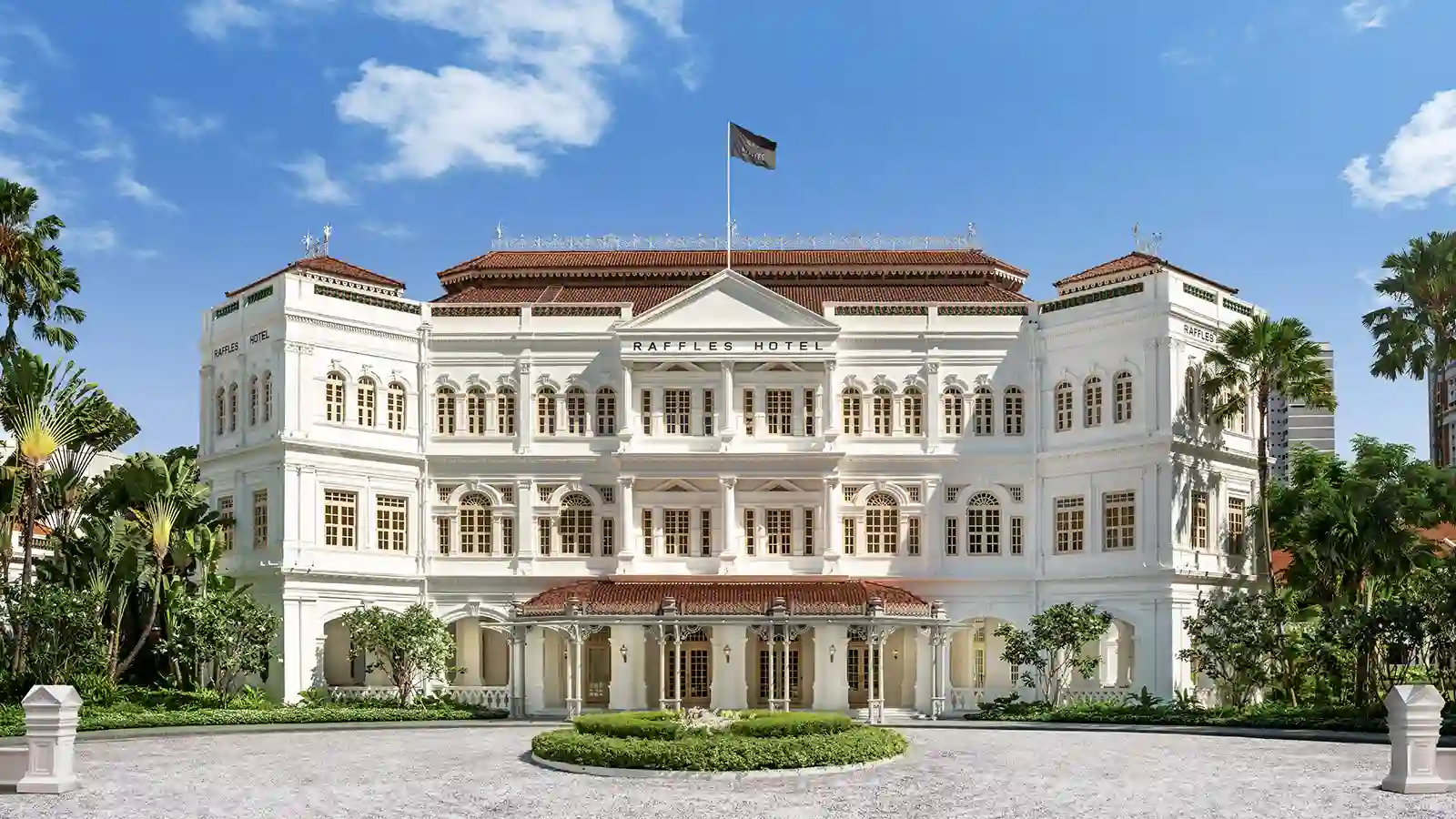 a large white building with a flag on top with Raffles Hotel in the background