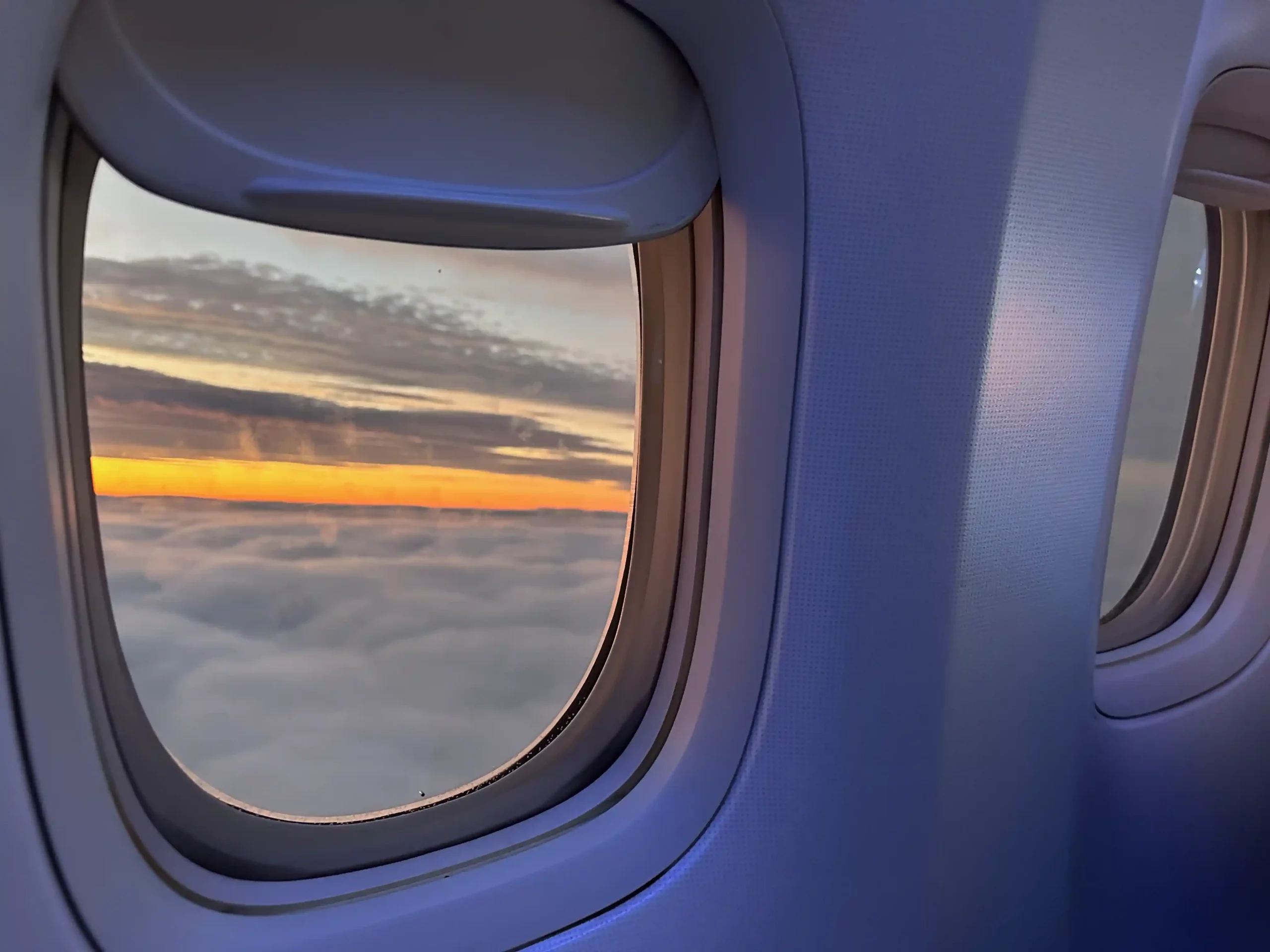 a window of an airplane with clouds and a sunset