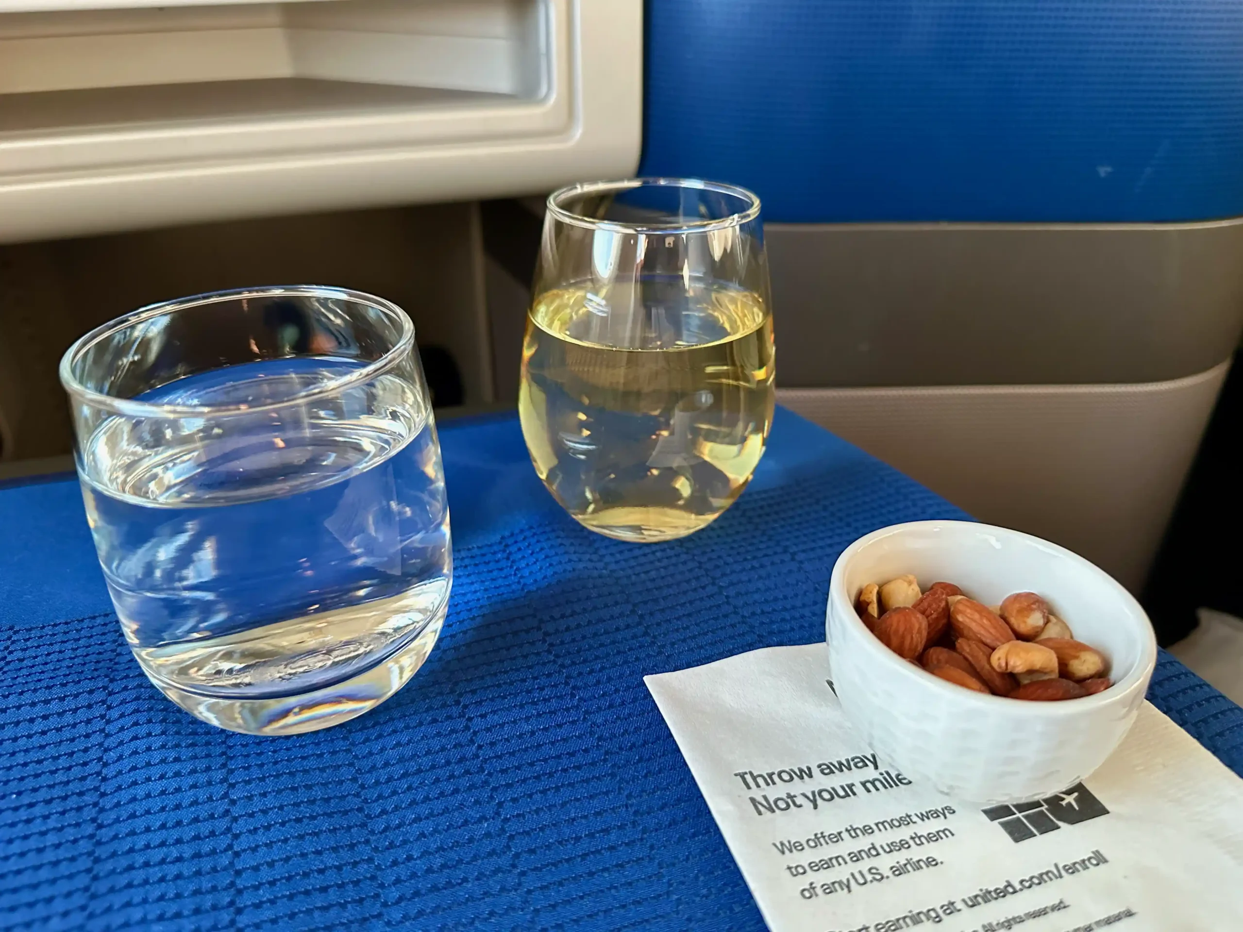 a glass of water and a bowl of nuts on a blue surface