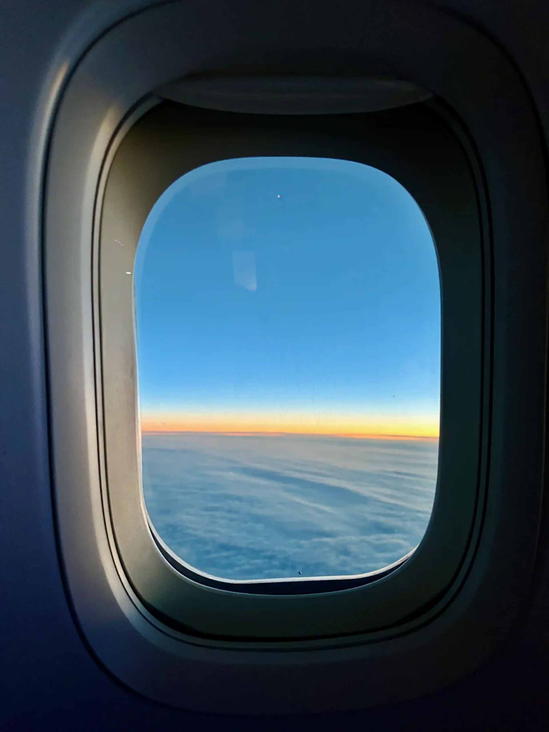 a window of an airplane with a view of the clouds and the sun