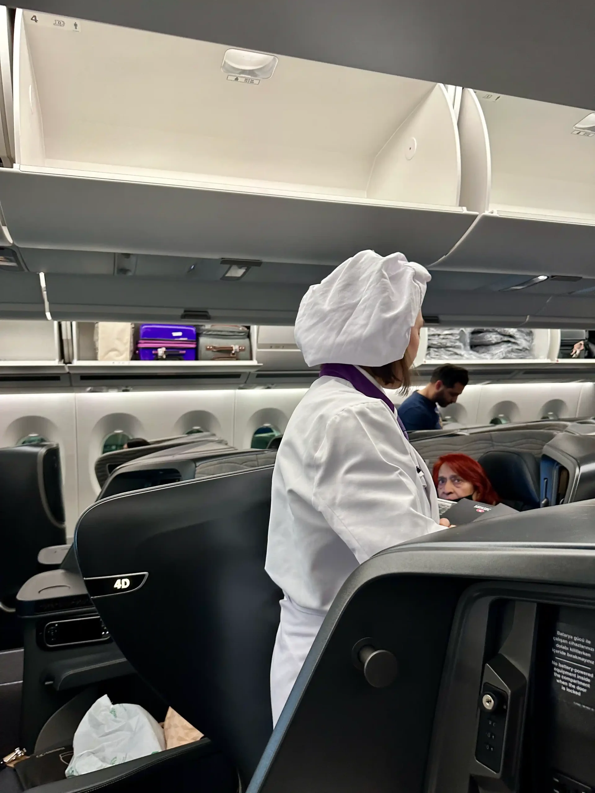 a woman in a white coat and white hat standing in an airplane